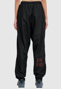 Czarne, luźne spodnie dresowe z elastyczną talią, bocznymi paskami i nadrukiem w czerwonym kolorze "DK 223" na lewej nodze. Gładka tekstura.
