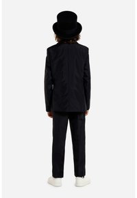 Black formal suit with a structured jacket and matching trousers, complemented by a tall black top hat and white sneakers.