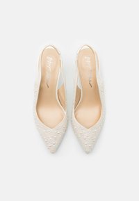 Pumps bianchi con tacco a sella e punta affilata, decorate con perline e con una soletta liscia. Ritagli trasparenti sui lati.