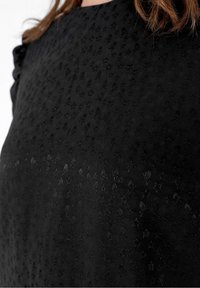 Tissu noir en gros plan sur un vêtement montrant un motif discret de crâne et d'étoile avec une finition texturée légèrement brillante et un détail froncé à l'épaule.