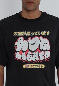 Black cotton t-shirt featuring bold, colorful Japanese text in varying fonts on the front, with a relaxed fit and short sleeves.