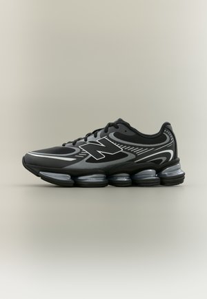 Scarpa da ginnastica atletica nera e grigia con suola segmentata imbottita, lacci e un grande logo "N" stilizzato sul lato.