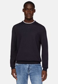 Dark navy knitted sweater with a ribbed texture, round neckline with white accent, and long sleeves, paired with light blue jeans.