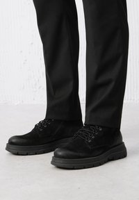 Czarne zamszowe buty o teksturowanej powierzchni, z masywną gumową podeszwą, z zapięciem na sznurowadła oraz subtelnym wykończeniem ściegów.