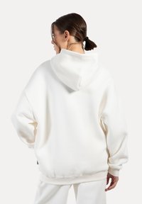 Hvid oversized hoodie med en stor hætte, ribbede manchetter og kant. Blød tekstur, minimal design, ingen synlige mønstre eller hardwaredetaljer.