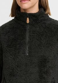 Pullover in pile nero con colletto alto, zip di lunghezza intermedia e superficie texturizzata e soffice. Presenta un tirazip in pelle beige.