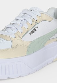 Baskets Puma blanches et beiges avec des lacets blancs, une bande latérale vert clair et une semelle blanche épaisse vues de profil.