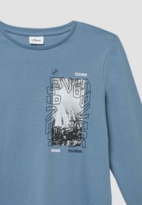 Hellblaues Langarm-T-Shirt aus einem Baumwollmix mit einem grafischen Design, das schwarz-weiße Elemente, Text und ein modernes Layout enthält.