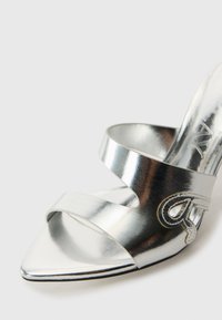 Zilveren hoge hakken sandaal met een spitse neus, kruislingse banden en gedetailleerde accenten. Gladde metallic leren afwerking met een glanzende textuur.
