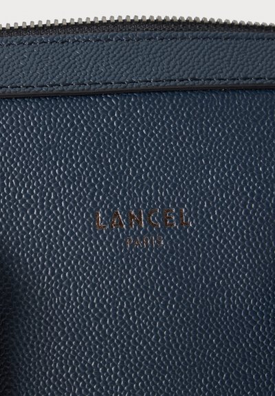 Текстурирана тъмносиня кожена повърхност с цип отгоре и "LANCEL PARIS" щамповани с златни букви.