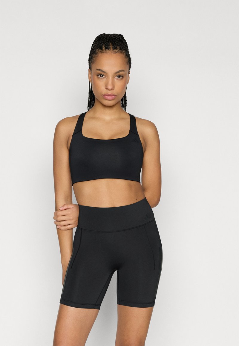 Zwarte atletische cropped top met een vierkante halslijn en brede bandjes, gecombineerd met hooggetailleerde, nauwsluitende zwarte shorts met zijkantennaden.