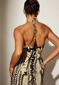 Femme aux cheveux en chignon portant un haut dos nu à motif noir et blanc noué d'un ruban et une jupe assortie, debout les mains sur les hanches.