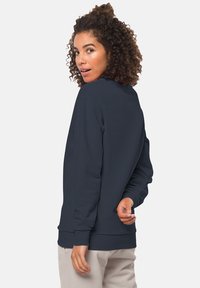 Felpa blu navy con maniche lunghe, scollatura rotonda e polsini a coste. Texture liscia e vestibilità casual, indossata con pantaloni chiari.