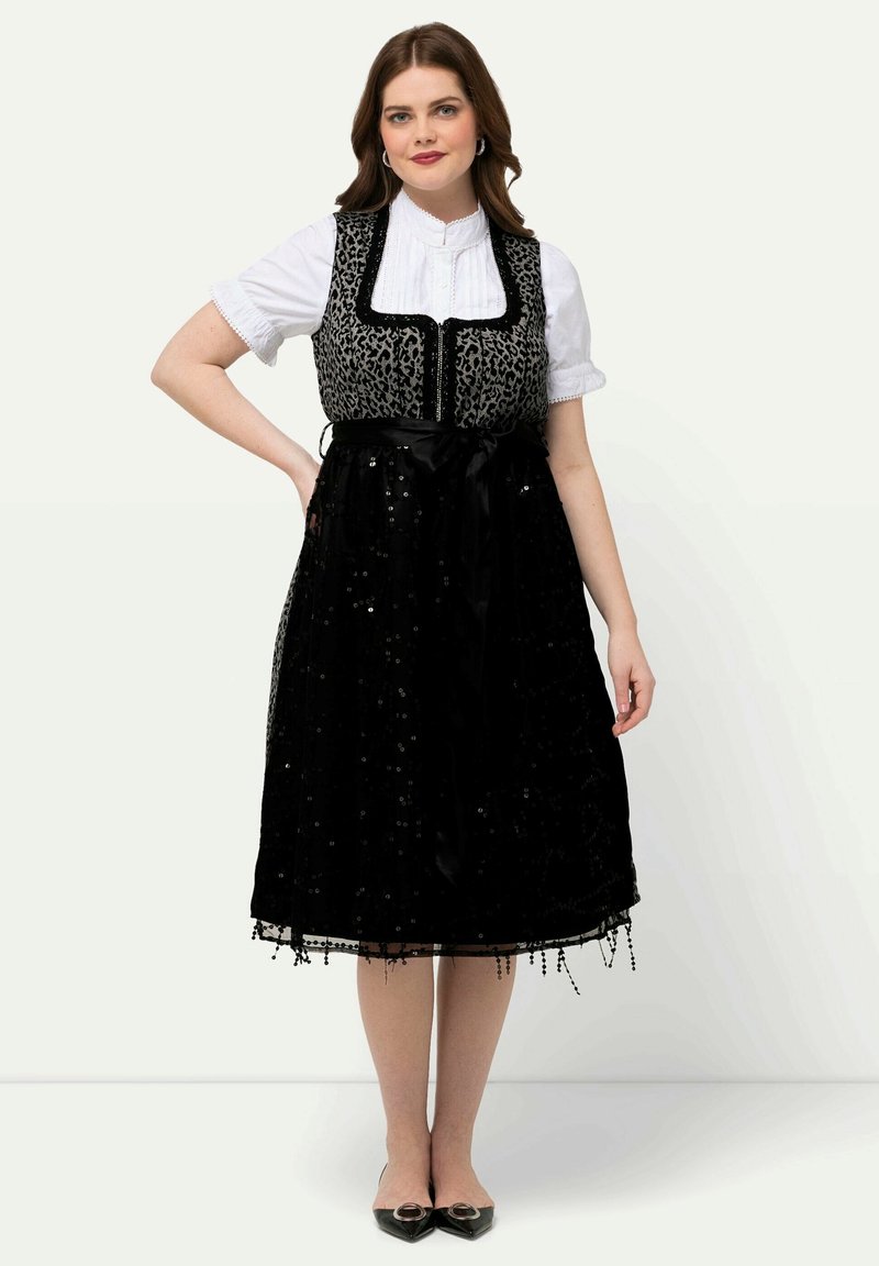 Vestido negro con lentejuelas, adornos de encaje y cinta de satén en la cintura; blusa blanca debajo; combinado con zapatos negros.