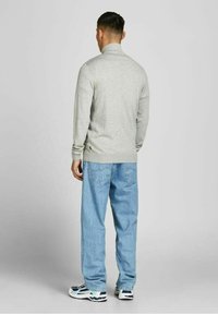 Světlý šedý pletený svetr s vysokým límcem, kombinovaný s volnými modrými džíny. Jednoduchý design bez viditelných vzorů, s ležérní estetikou.