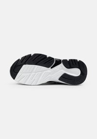Semelle de chaussure de sport noir et blanc, avec un caoutchouc épais au motif texturé, des rainures pour l'adhérence et une semelle intermédiaire blanche solide.