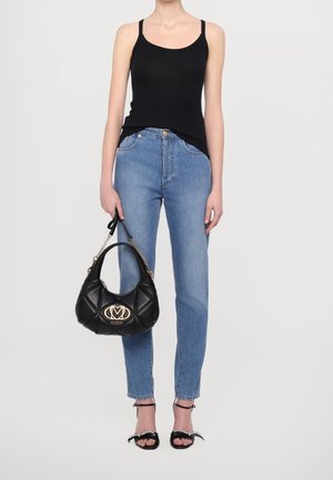 Schwarzes Tanktop, hellblaue Jeans und schwarze Handtasche mit gesteppter Textur und goldenen Beschlägen. Schwarze Sandalen mit dekorativen Schleifen.