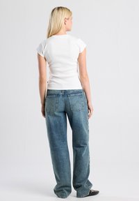 White, short-sleeve fitted top paired with relaxed-fit, light blue denim jeans featuring back pockets and a straight-leg design.