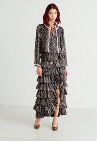 Leopardmønster kjole med rynkede lag, med krage og kontrastfarget slips. Stoffet er lett og har en flytende silhuett.
