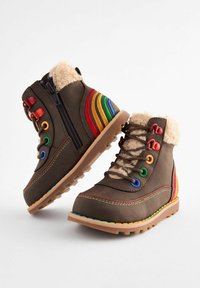 Stivali alla caviglia marroni con un morbido colletto in pelliccia sintetica, occhielli colorati e un design con strisce arcobaleno sui lati. Suola in gomma con battistrada per una buona presa.