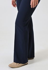Marineblauwe flared broek gemaakt van zachte, rekbare stof, gecombineerd met beige suède loafers met een kleine hardwareaccent.