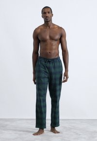 Zelené kárované pohodlné nohavice z mäkkého materiálu s elastickým pásom a šnúrkou, ktoré majú voľný strih. Bez vreciek a viditeľných kovových doplnkov.