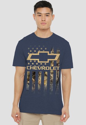 Navy blue cotton t-shirt featuring a gold Chevrolet logo and American flag design with a camo pattern overlay in the stripes.