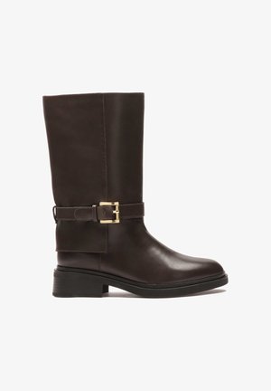 Botte haute en cuir marron avec une pointe arrondie, une semelle noire épaisse et une boucle dorée décorative sur la sangle de la cheville.