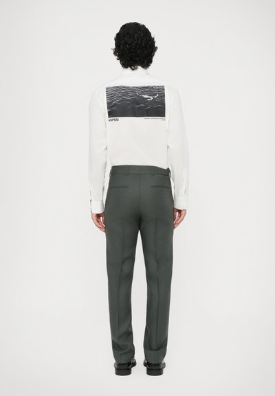 Camicia bianca a maniche lunghe con grafica nera sul retro, abbinata a pantaloni su misura verde scuro. Design minimalista con linee pulite.