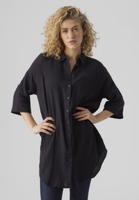 Camicia nera button-up in tessuto testurizzato, con vestibilità comoda, maniche arrotolate e orlo curvo, abbinata a jeans scuri.