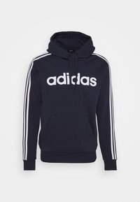 Hoodie bleu marine avec le logo Adidas blanc et trois bandes blanches le long de chaque manche. Comprend une poche kangourou et une capuche avec cordon.