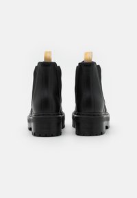 Botine negre până la gleznă, cu un finisaj din piele netedă, panouri din plasă texturată, tălpi groase din cauciuc și bucle galbene la spate.
