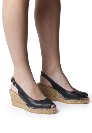 Black leather wedge shoes with open toe, slingback strap, and woven jute detailing on the sole. Stitched accents highlight the design.