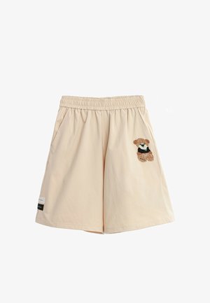 Pantalones cortos beige con cintura elástica y bolsillos laterales, decorados con un pequeño oso de peluche bordado en el lado derecho y dos etiquetas de tela cerca del dobladillo izquierdo.