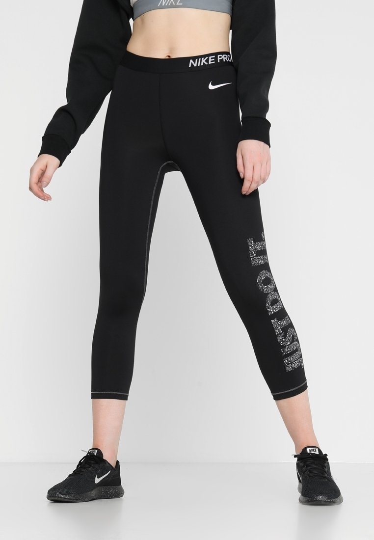 Femme portant un legging Nike Pro noir avec un logo blanc sur la taille et un texte tacheté « Just Do It », associé à des baskets Nike noires.
