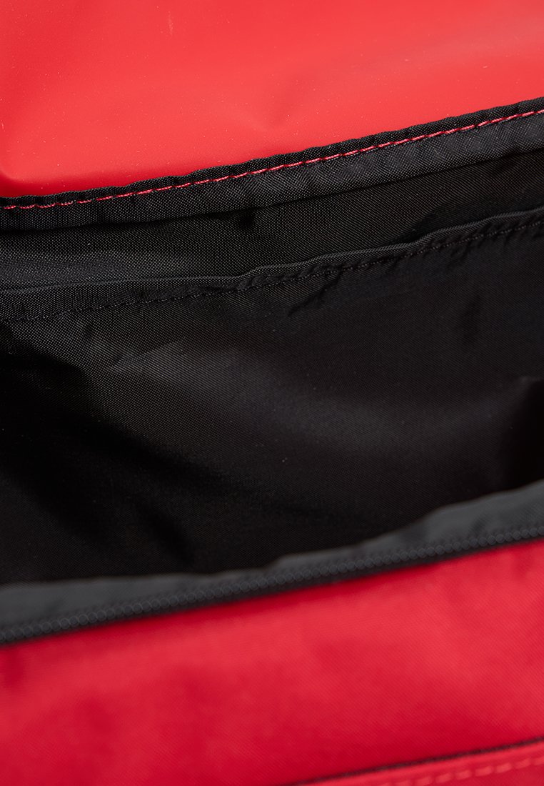 Bolso rojo con un exterior suave y un interior de tela negra, con cierre de cremallera y costuras rojas contrastantes a lo largo de la costura.