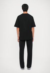 Μαύρο κοντομάνικο πουκάμισο με χαλαρή εφαρμογή, συνδυασμένο με μαύρα παντελόνια. Και τα δύο είναι φτιαγμένα από ελαφρύ υλικό, χωρίς ορατά σχέδια ή γραφικά.