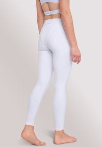 Witte legging van rekbaar materiaal, met een hoge taille en een naadloos ontwerp. Gladde textuur met minimale branding op de tailleband.