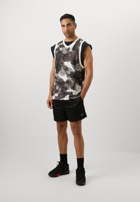 Top sin mangas con patrones abstractos en gris y negro, combinado con pantalones cortos negros y zapatos negros; presenta un cuello redondo y amplias sisas.