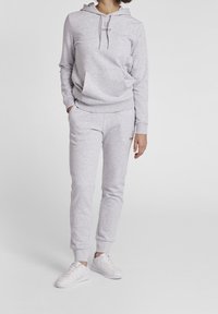 Grå hoodtröja med framficka och dragsko, ihop med matchande svettbyxor. Slät textur, ribbade muddarna. Vita sneakers kompletterar outfiten.