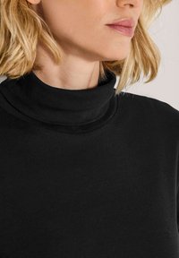 Schwarzer Rollkragenpullover aus weichem Stoff, mit hohem Kragen und glatter Textur. Nahaufnahme, die die Passform am Halsausschnitt und Kragen zeigt.