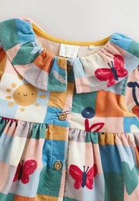 Robe en velours côtelé présentant un motif en patchwork multicolore avec des papillons et un soleil, un col volanté et des accents de boutons en bois.