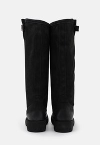 Bottes hautes jusqu'au genou en daim noir avec semelles en caoutchouc plates noires, présentant des coutures verticales et des sangles ajustables en haut. Texture lisse.