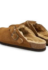 Zoccoli in suede marrone con una morbida fodera in pelliccia, cinturino regolabile con fibbia in metallo e suola in sughero texturizzata. Presentano un design ampio e aperto.