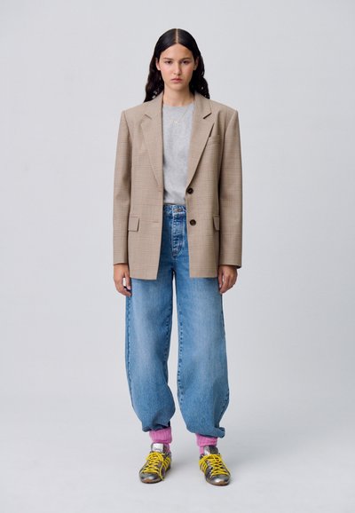 Blazer overdimensionato a quadri beige, t-shirt grigia, jeans blu a vita alta, calzini rosa, sneakers metalliche con lacci gialli.