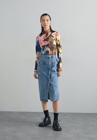 Ένα πολύχρωμο μπλουζάκι με μακριά μανίκια και αφηρημένα λουλουδάτα σχέδια, σε συνδυασμό με μια τζιν φούστα ψηλόμεση. Μαύρα παπούτσια με κορδόνια και κάλτσες μέχρι τον αστράγαλο ολοκληρώνουν την εμφάνιση.