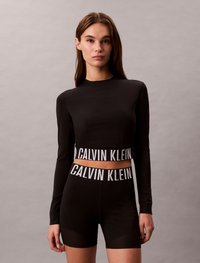 Melna garu piedurkņu krekls un šorti ar kontrastējošu balto "CALVIN KLEIN" zīmolu jostasvietas daļā; gluda tekstūra, pieguļoša dizains.