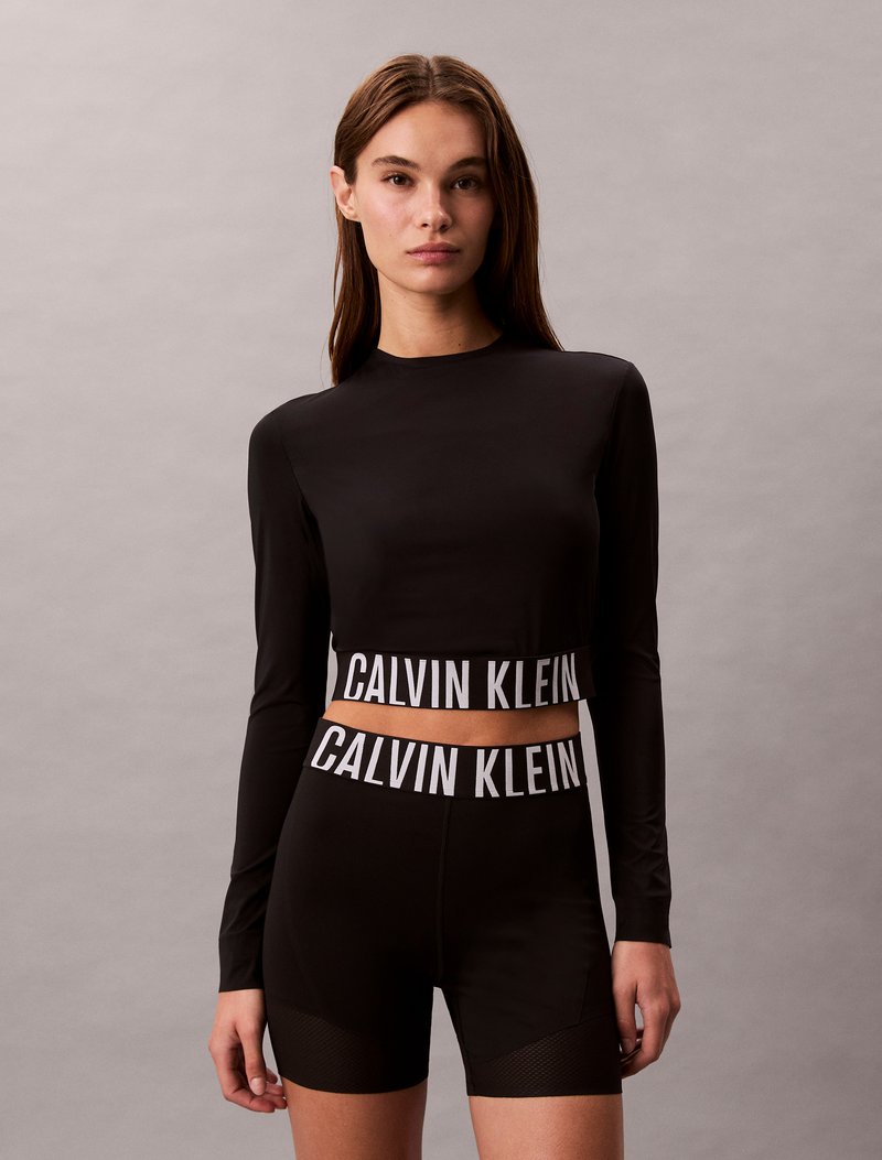 Melna garu piedurkņu krekls un šorti ar kontrastējošu balto "CALVIN KLEIN" zīmolu jostasvietas daļā; gluda tekstūra, pieguļoša dizains.