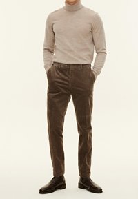 Beige Rollkragenpullover kombiniert mit braunen Cordhosen. Das Outfit präsentiert sich in einer schmalen Passform, mit glatter Textur und einem dezenten Rippmuster. Braune Lederstiefel.