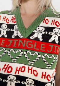 Strickweste aus hochwertigem Material mit V-Ausschnitt. Das Design zeigt Lebkuchenmänner, Zuckerstangen und Schriftzüge in Rot und Grün auf schwarzem Hintergrund.